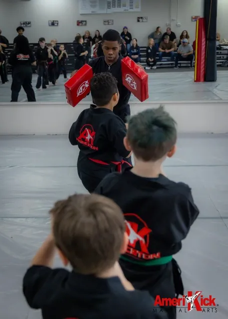Kids Martial Arts students lined up taking turns kicking pads held by instructor